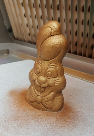 coniglietto di cioccolato colorato con spray oro sul tavolo di un laboratorio di pasticceria