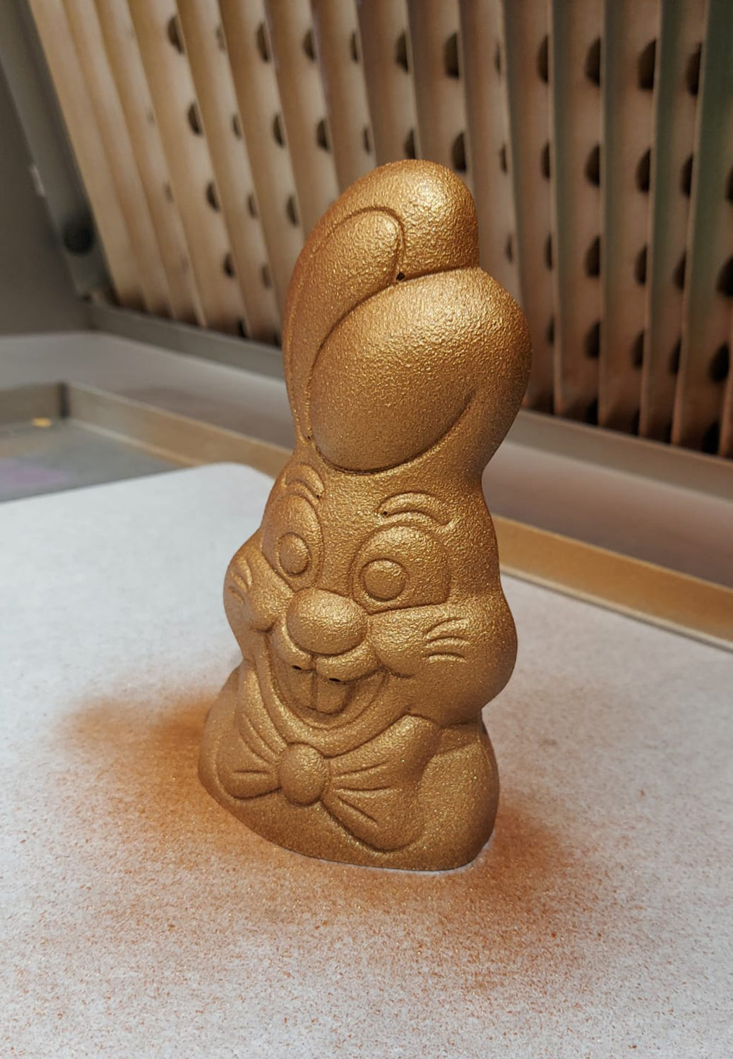 coniglietto di cioccolato colorato con spray oro sul tavolo di un laboratorio di pasticceria