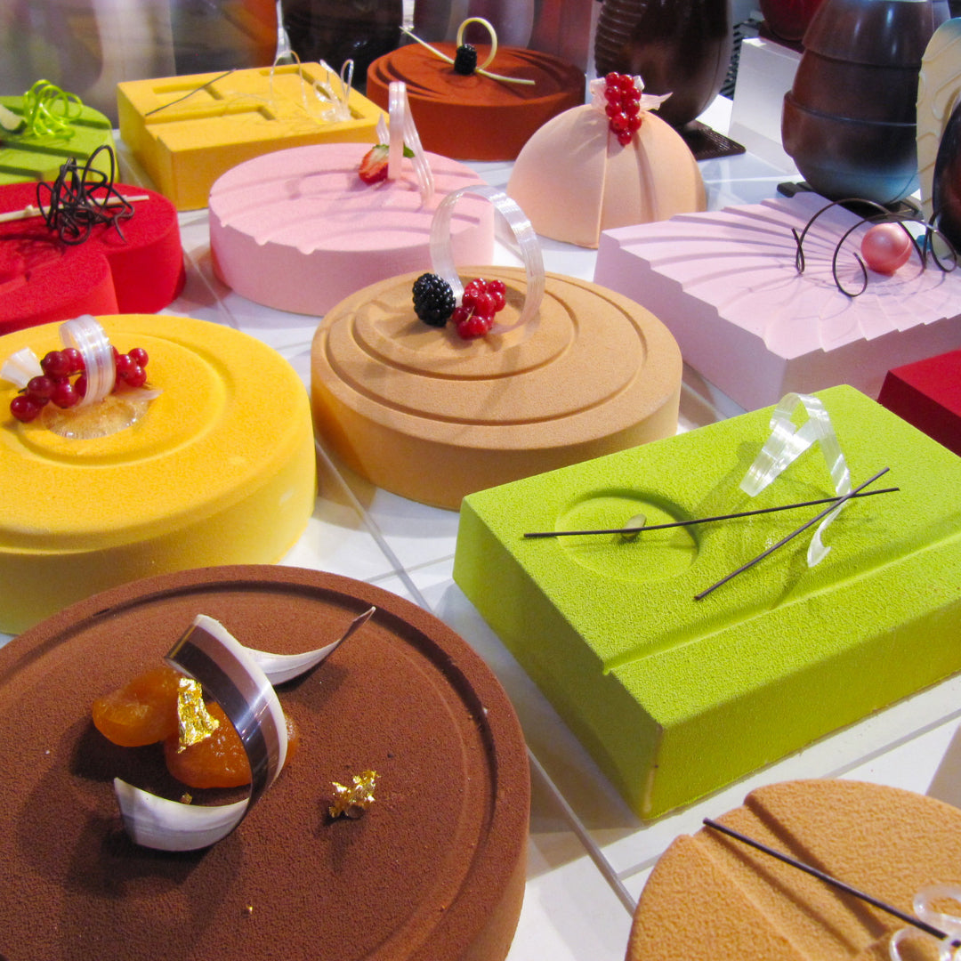 Varie torte di diversi colori, forme e decorazioni. Sono tutte rivestite con colore ad effetto velluto. Sono posizionate su un piano bianco