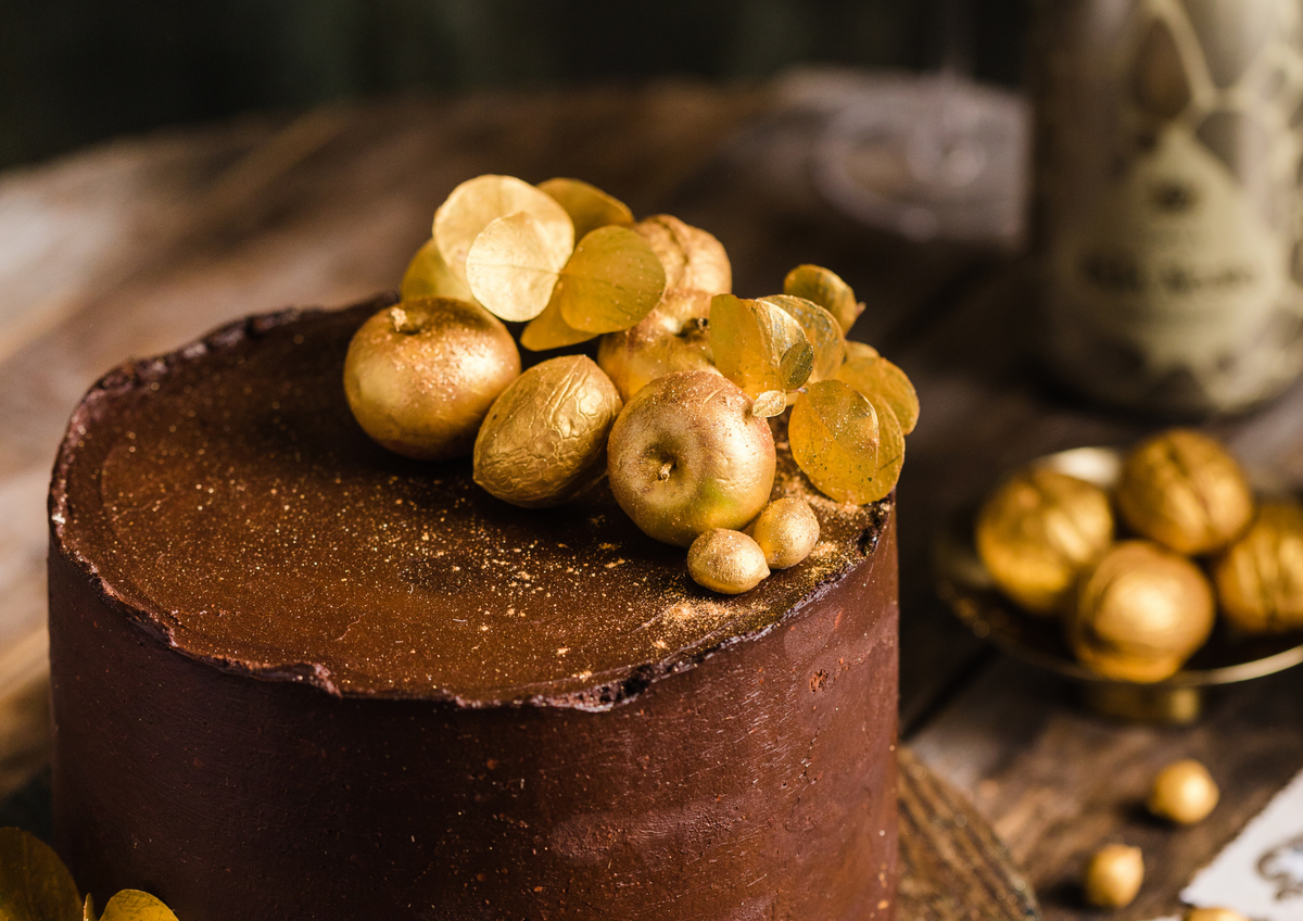 Torta di cioccolato su ripiano di legno, sfondo sfocato, sul dolce una decorazione di frutta completamente rivestita di spray oro