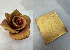 Due figure di cioccolato appoggiate su carta forno, una rosa con una velatura di spray oro e un quadretto con colore oro coprente