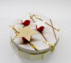 Torta bianca con bordo rivestito di quadretti di cioccolato bianco. Effetto vellutato bianco in superficie, con decorazione di foglietti d'oro, 3 lamponi sormontati da tre stelle di cioccolato bianco di cui una dorata.
